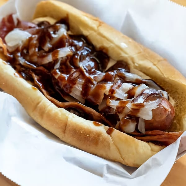 El Capitan's hot dog with bacon, onions, and barbecue sauce in a white paper tray.