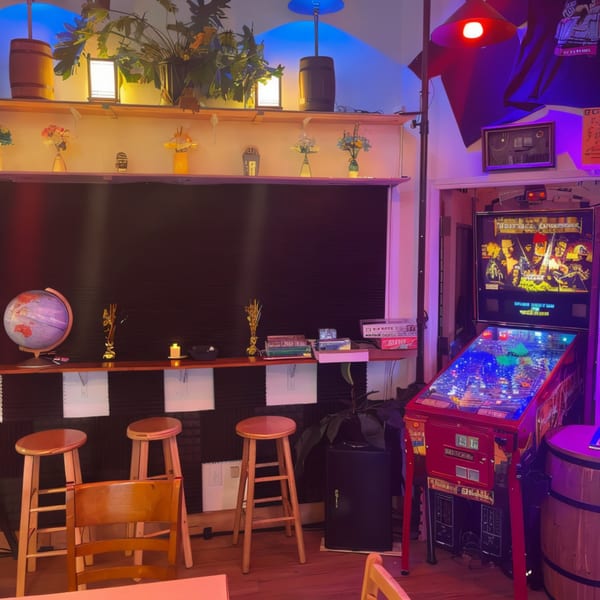 A dimly lit El Capitan's interior with a pinball machine, bar stools, and decorative shelves.